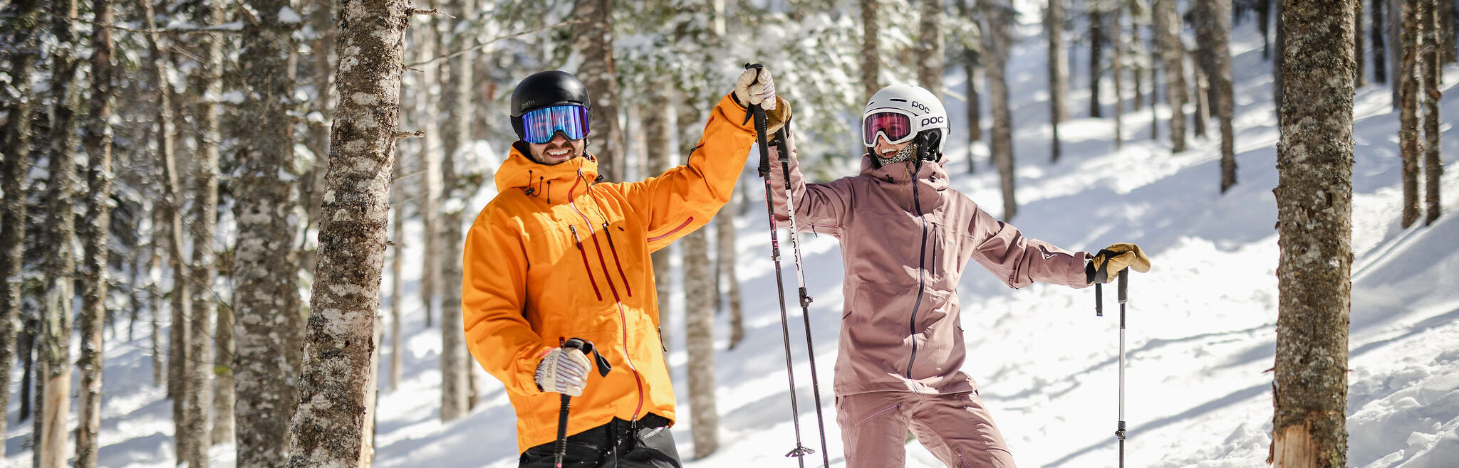 Skier in orange jacket and skier in light purple jacket high five